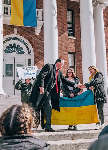 BSU President Fred Clark shaking hands with students holding the Ukrainian flag in front of Boyden Hall; a man holds a sign that says Freedom for Ukraine